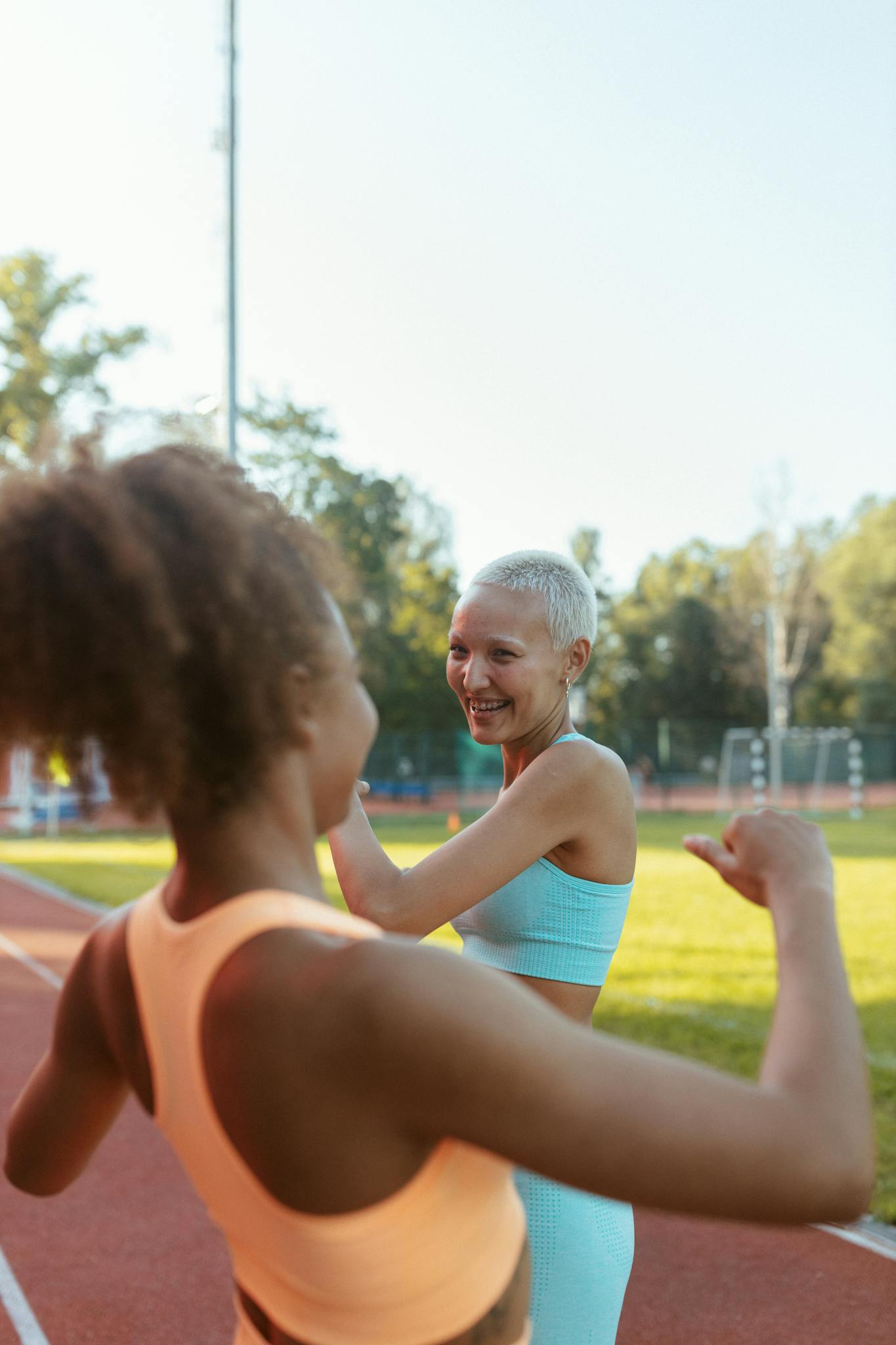 Two women in activewear exercising on a running track outdoors, smiling and enjoying the activity.